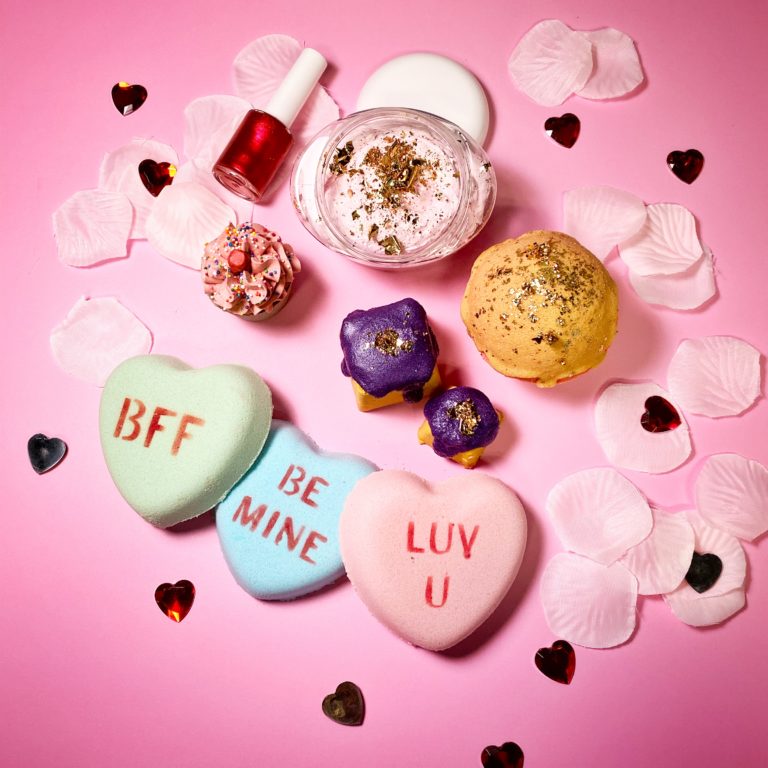 Red nail polish, a gold bath bomb, purple bubble bars, and candy heart bath bombs that say